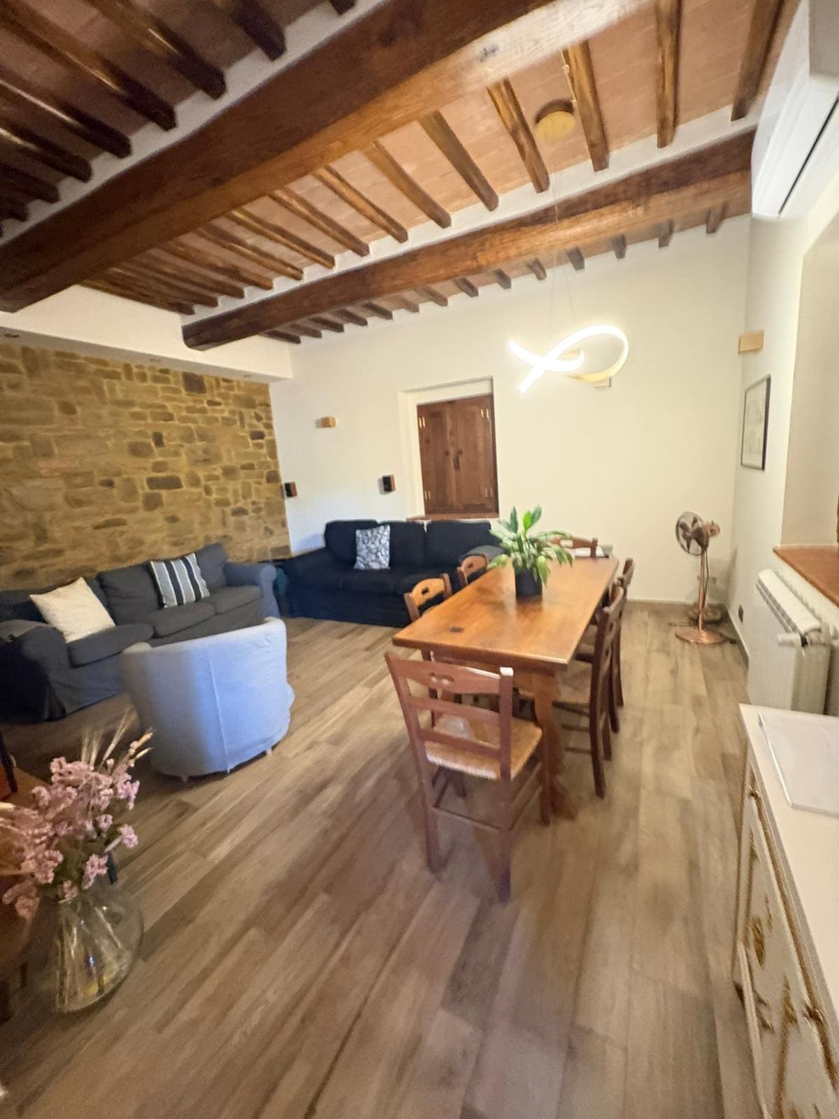 Soggiorno con travi a vista, parete in pietra e tavolo in legno massello de La Dimora del Vino a Buonconvento dopo intervento J&D Clean Service.